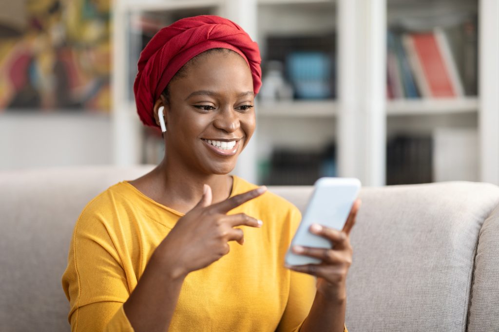 Cheerful african american lady using cell phone and earpods