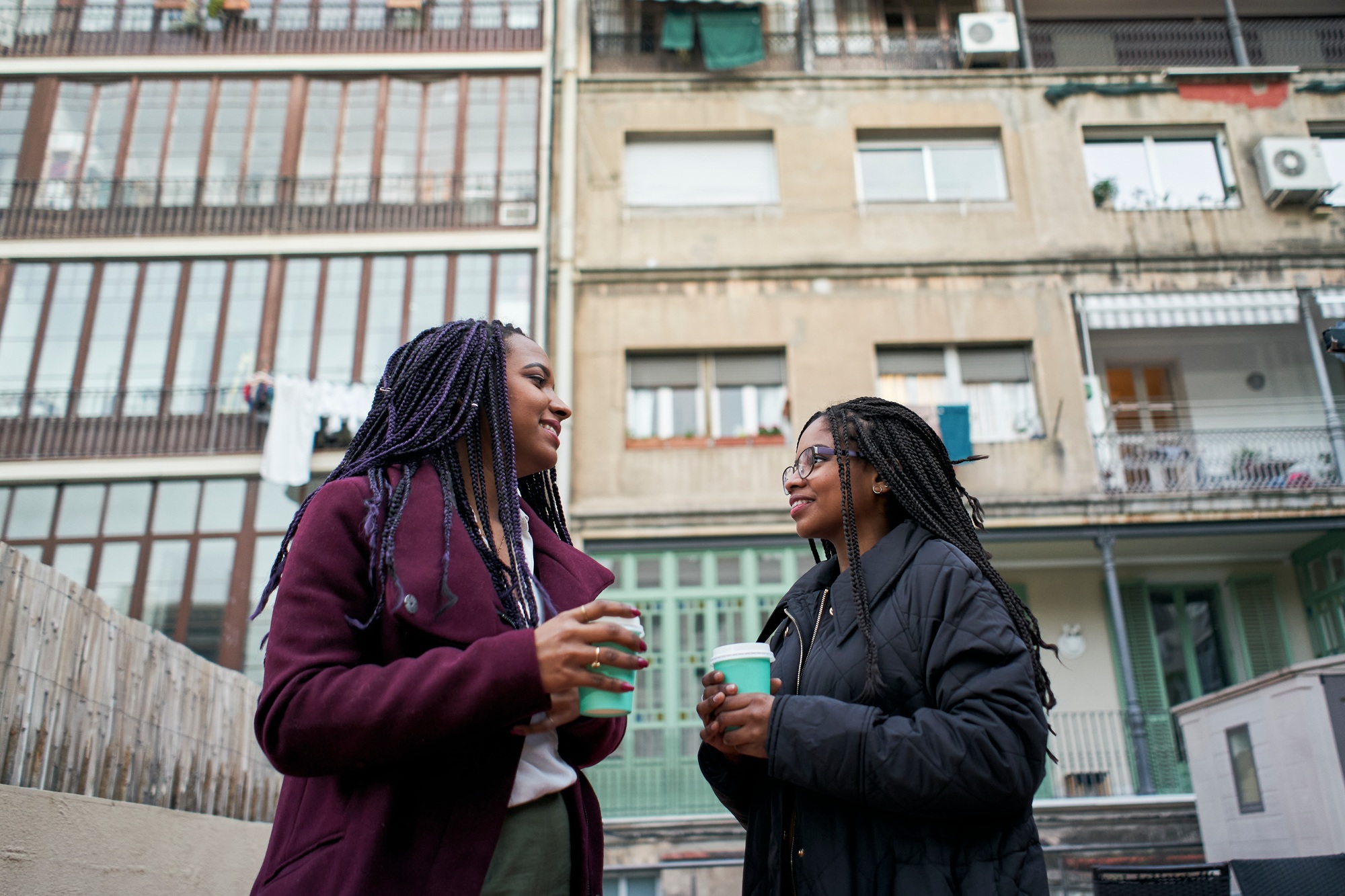 Two young African American business women using a phone and holding a coffee outside.